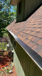 roof inspection likely by wishnwash services showing detailed shingles and gutters with green siding in the background